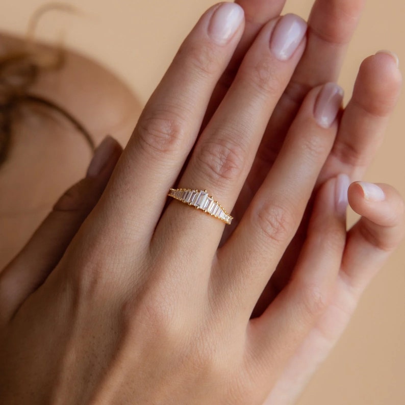 May include: A gold band ring with a row of baguette-cut diamonds set in a graduated pattern.