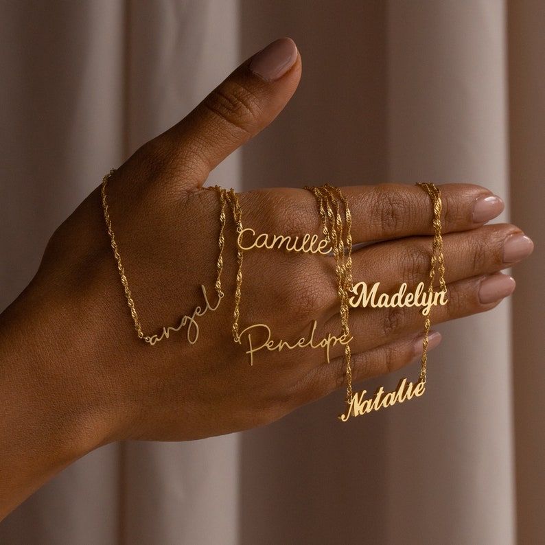 May include: Five gold necklaces with different names on them: 'Angel', 'Camille', 'Madelyn', 'Penelope', and 'Natalie'.