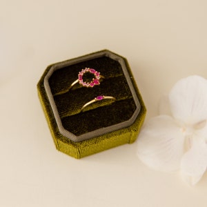 May include: Two gold rings with pink gemstones in a green velvet ring box. The larger ring has a circle of pink gemstones. The smaller ring has a single pink gemstone.