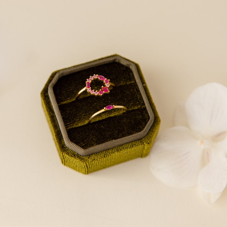 May include: Two gold rings with pink gemstones in a green velvet ring box. The larger ring has a circle of pink gemstones. The smaller ring has a single pink gemstone.