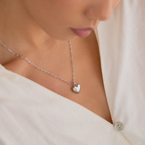 May include: A silver chain necklace with a heart-shaped pendant. The pendant is smooth and shiny.