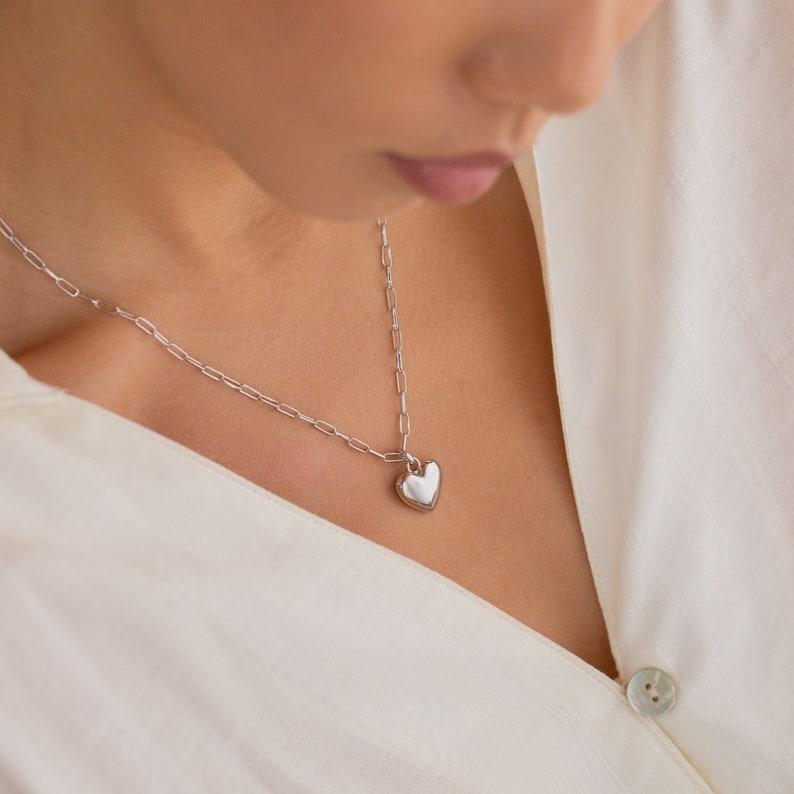 May include: A silver chain necklace with a heart-shaped pendant. The pendant is smooth and shiny.
