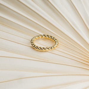 May include: A gold-colored ring featuring a continuous twisted rope design. The band has a polished, reflective surface that catches the light, creating a uniform, circular shape with a repeating spiral pattern throughout the entire circumference.