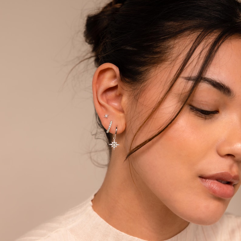 May include: A close-up of a person's ear with multiple earrings. The earrings are silver and have a star design. The earrings are worn in the lobe and helix piercings.