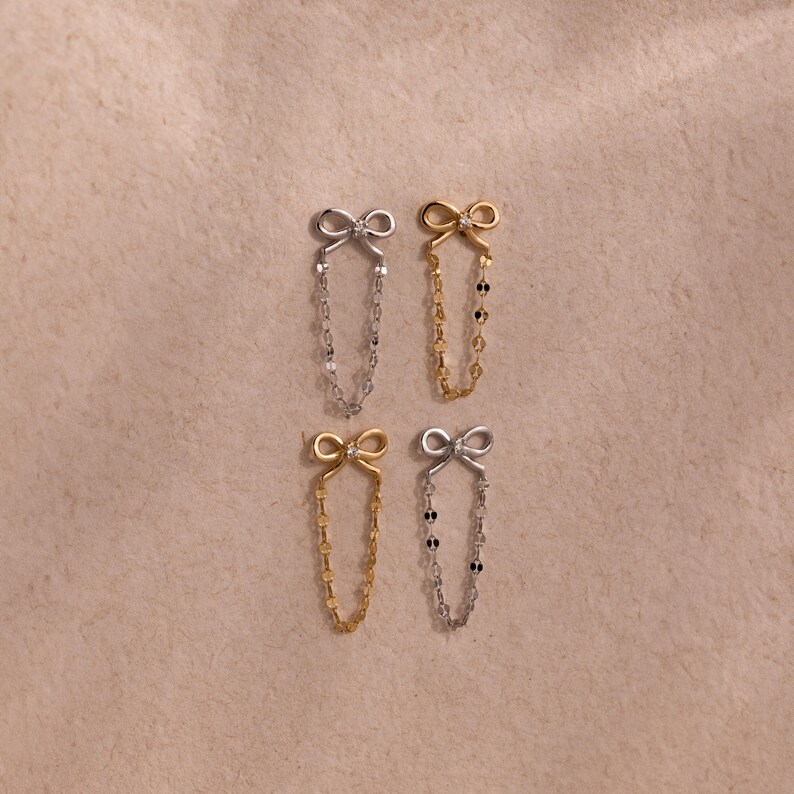 Set of Bow Chain Stud Earrings in gold and silver finishes, each featuring delicate bow studs with draped chain loops, displayed on a textured neutral background.