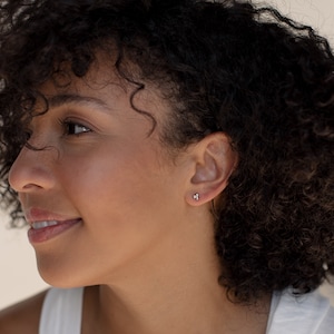 May include: A close-up of a person's ear with a small, silver stud earring. The earring has three small, round stones.