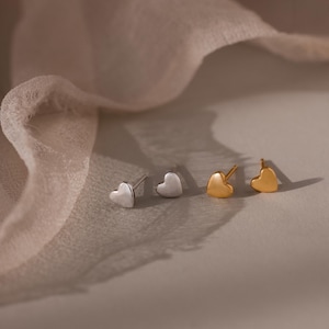 May include: Two pairs of heart-shaped stud earrings, one pair in a polished silver tone and one pair in a polished gold tone. Each earring features a simple, smooth heart design with a post back, presented as small, minimalist jewelry pieces.