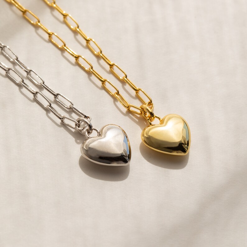 May include: Two delicate necklaces with heart-shaped pendants. One necklace has a gold chain and a gold heart pendant, while the other has a silver chain and a silver heart pendant.