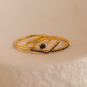 May include: Three gold rings with black stones and white accents. The rings are stacked on top of each other.