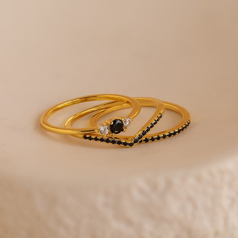May include: Three gold rings with black stones and white accents. The rings are stacked on top of each other.