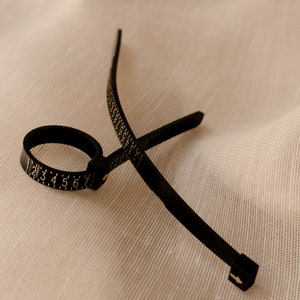 May include: A black plastic ring sizer with a numbered scale from 1 to 7. The sizer is flexible and can be adjusted to fit different finger sizes.
