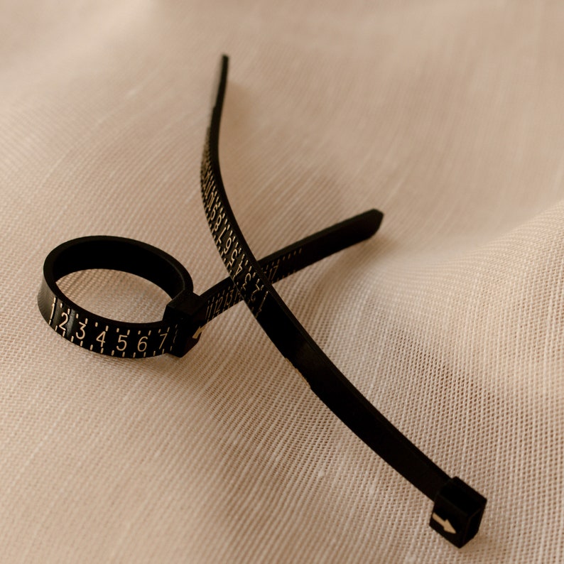 May include: A black plastic ring sizer with a numbered scale from 1 to 7. The sizer is flexible and can be adjusted to fit different finger sizes.