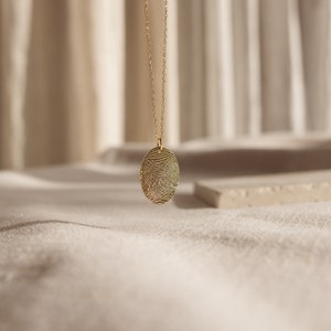 May include: A gold chain necklace with an oval pendant featuring a detailed fingerprint design.