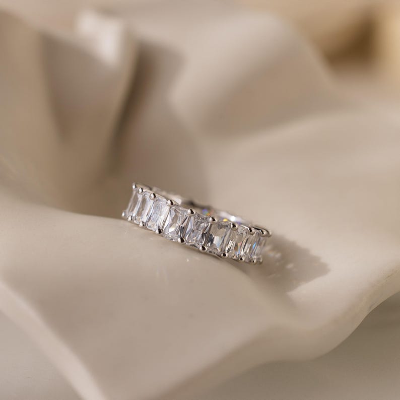 May include: A silver ring with a row of clear rectangular stones.