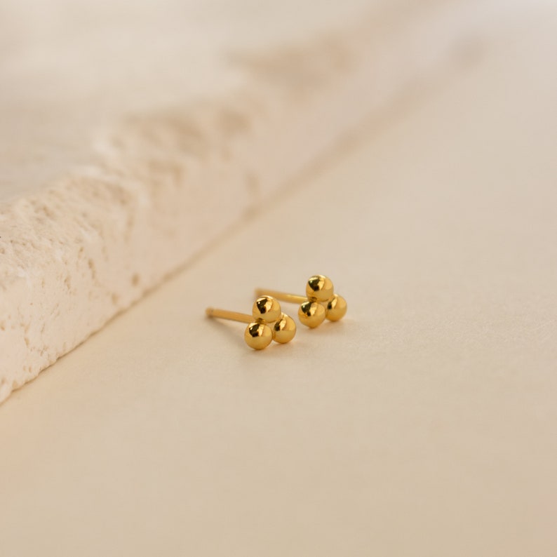 May include: A pair of gold stud earrings with three small round balls on each earring.