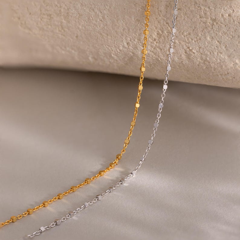 Close-up of two Dot Station Necklaces in silver and gold, each featuring a dainty beaded chain design.