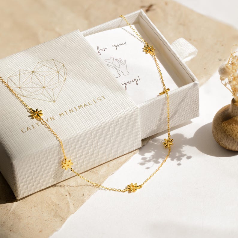 May include: A gold chain necklace with small flower charms. The necklace is in a white box with a handwritten note that says "for you!" and "joy!"