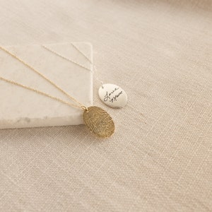 May include: Two silver necklaces with oval pendants. One pendant features a fingerprint design and the other has the handwritten text "Love Mom".