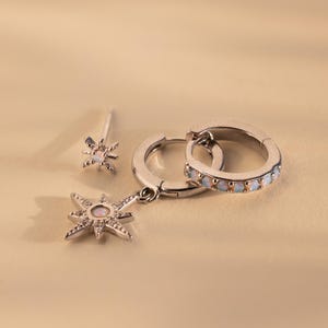 May include: A set of three silver earrings featuring a starburst design with opal accents. The earrings include a pair of hoop earrings and a single stud earring.