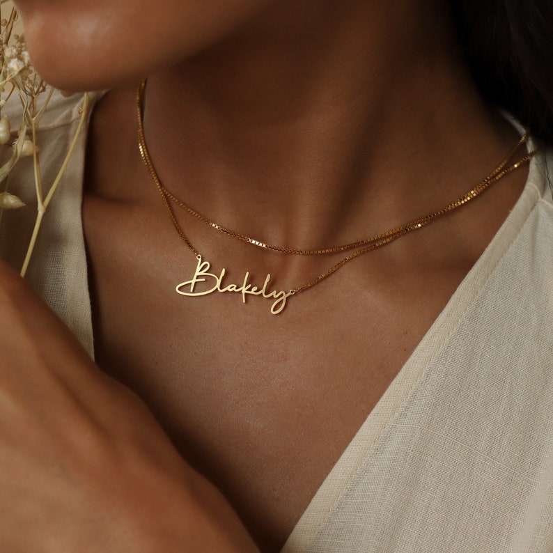 May include: A gold chain necklace with a cursive nameplate pendant that says 'Blakely'