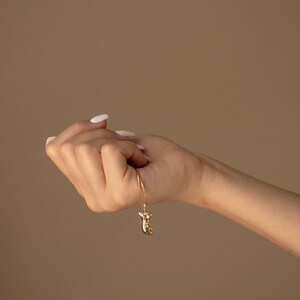 May include: A gold chain necklace with a gold pendant shaped like a stylized human figure.
