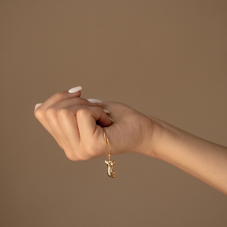 May include: A gold chain necklace with a gold pendant shaped like a stylized human figure.
