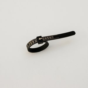 May include: Black plastic ring sizer with gold numbers 6 to 17 and an arrow pointing to the right.