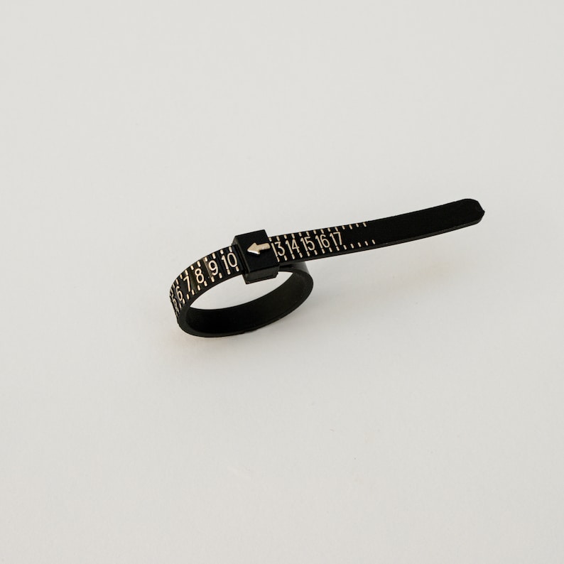 May include: Black plastic ring sizer with gold numbers 6 to 17 and an arrow pointing to the right.