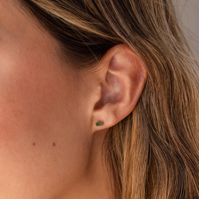 K&ouml;nnte beinhalten: Nahaufnahme eines Ohrs mit einem kleinen gr&uuml;nen Edelstein-Ohrring.
