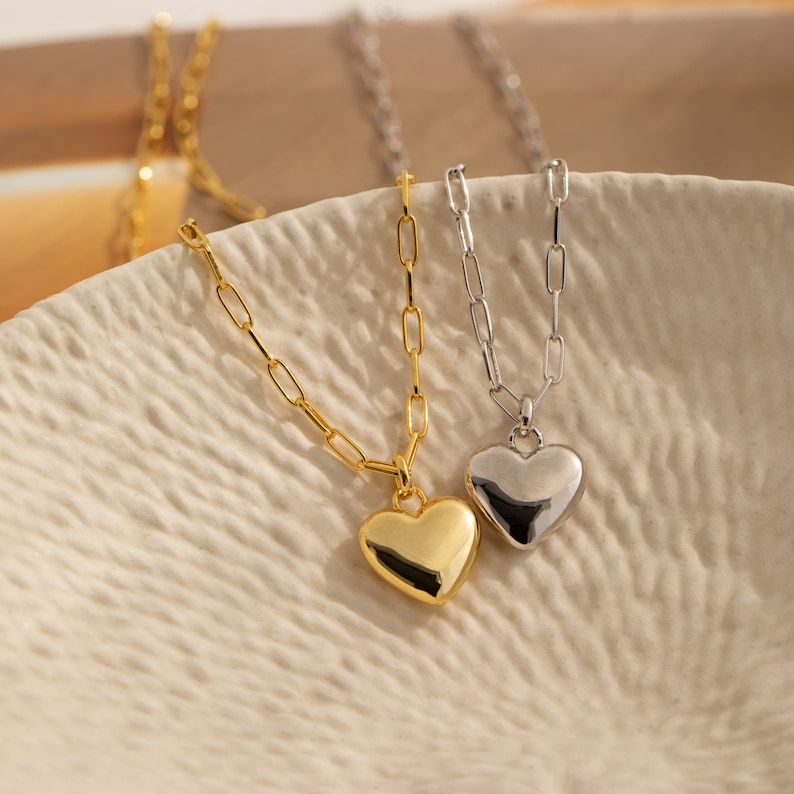 May include: Two gold and silver necklaces with heart pendants. The gold necklace has a larger heart pendant than the silver necklace.
