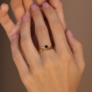 May include: Three gold rings with black and white stones. The top ring features a square black stone, the middle ring has a row of small white stones, and the bottom ring has a row of small black stones.