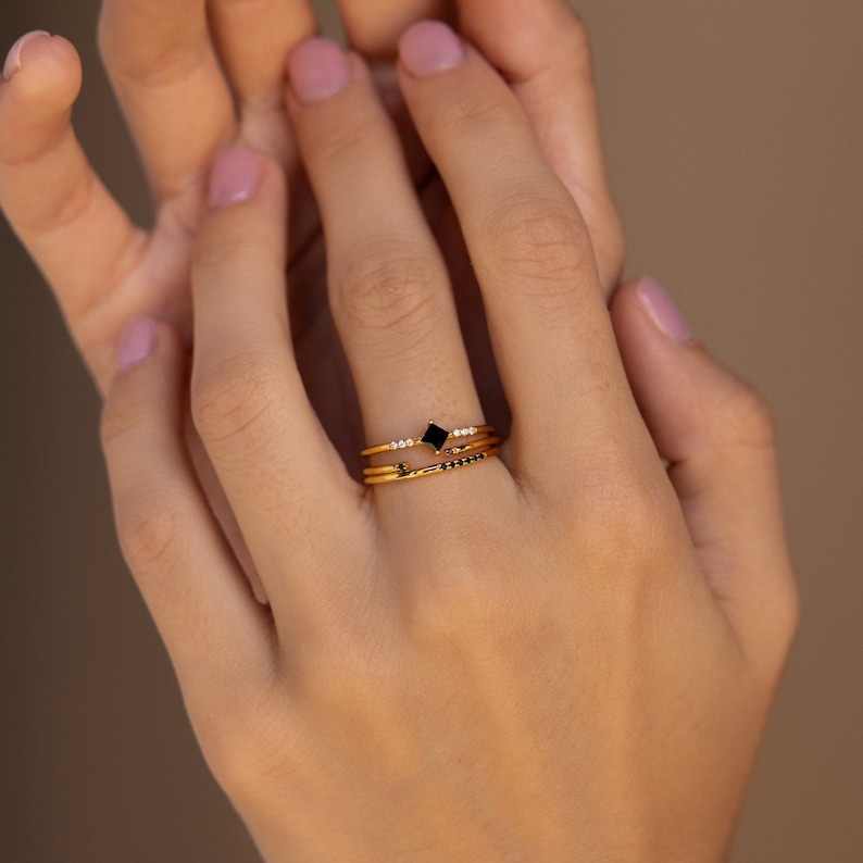 May include: Three gold rings with black and white stones. The top ring features a square black stone, the middle ring has a row of small white stones, and the bottom ring has a row of small black stones.