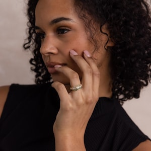 May include: A stack of gold rings with intricate detailing. The rings feature a mix of textures and designs, including what appears to be small gemstones. The rings are worn on a finger, showcasing the jewelry's craftsmanship and elegance.