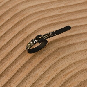 May include: Black ring sizer with gold numbers 3 to 17 printed on it. The sizer is made of flexible plastic and has a small arrow pointing to the right.