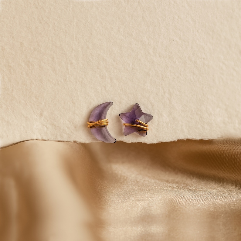 May include: A pair of earrings featuring a crescent moon and a star, both made of amethyst and wrapped in gold wire.