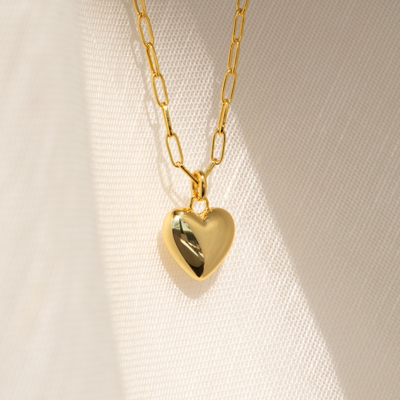May include: A gold chain necklace with a large, solid gold heart pendant.