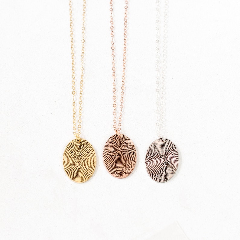 May include: Three necklaces with oval pendants featuring fingerprint designs. The necklaces are gold, rose gold, and silver.