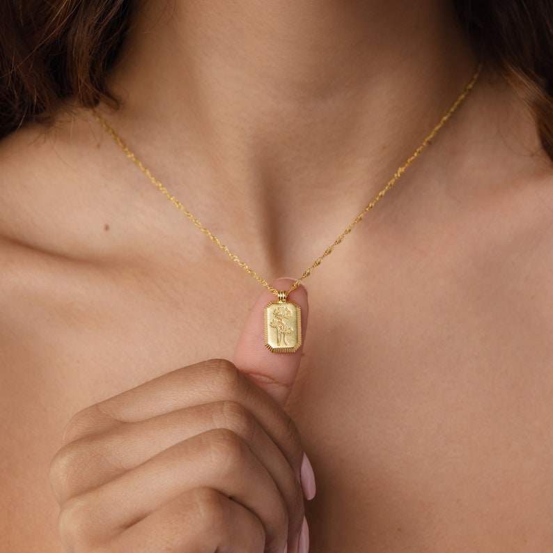 A gold twist chain has a rectangle pendant with an engraved flower on it. There are lines engraved along the outside of the charm and in the middle there is a daisy flower engraved design.