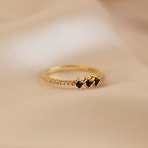 May include: A gold band ring with a row of small clear stones and three black square-shaped stones.