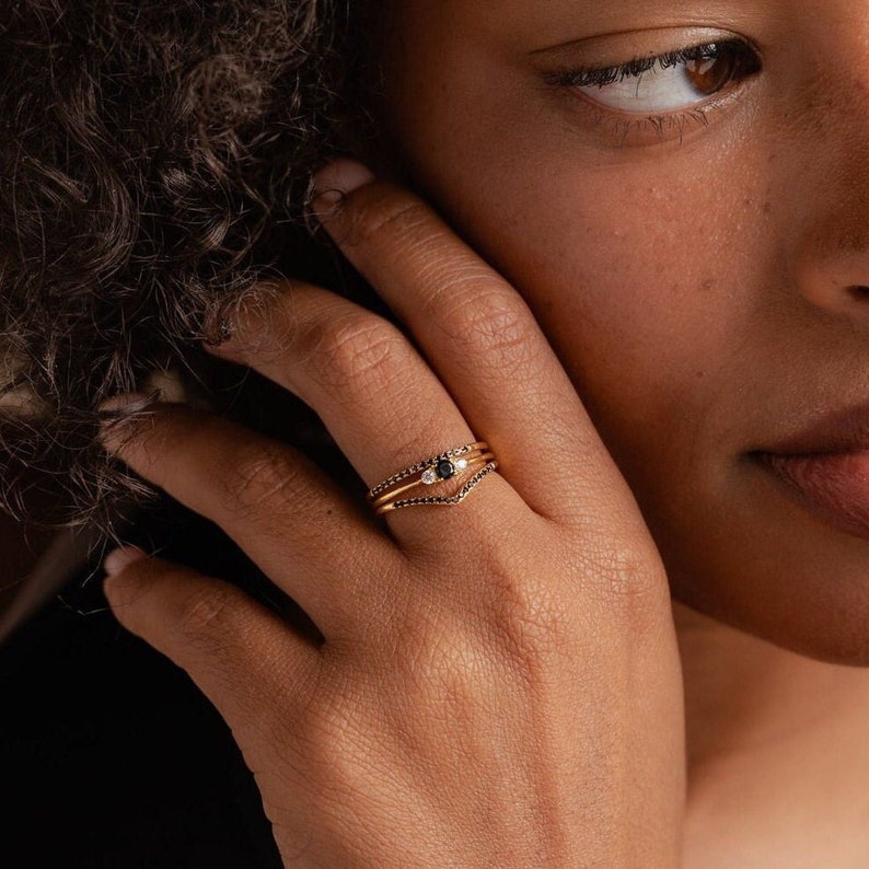 May include: A set of three gold rings with black and white gemstones. The rings are stacked on a finger.