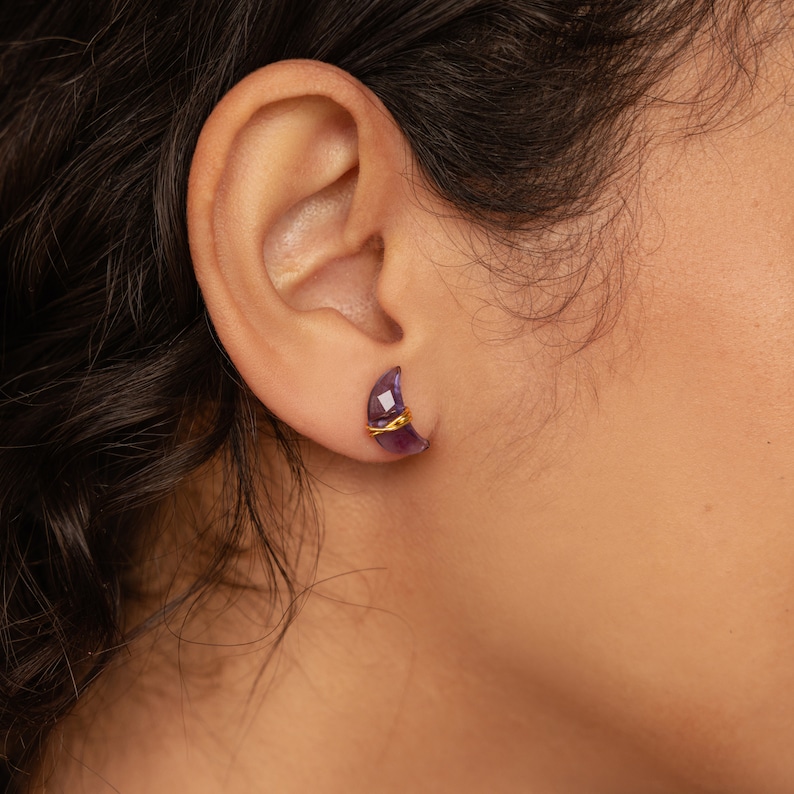 May include: A pair of crescent moon shaped earrings with a purple gemstone and gold wire accents.
