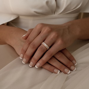 May include: A gold band ring with a row of clear rectangular stones.