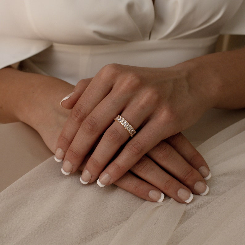 May include: A gold band ring with a row of clear rectangular stones.