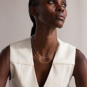 Model wearing the Dot Station Necklace in gold, featuring a dainty beaded chain design, layered with a matching gold chain necklace.