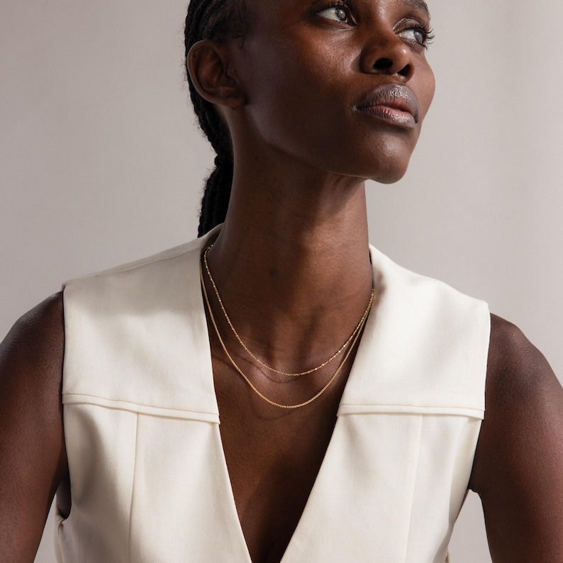 Model wearing the Dot Station Necklace in gold, featuring a dainty beaded chain design, layered with a matching gold chain necklace.