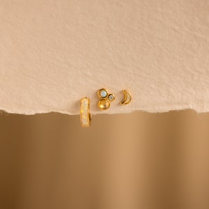 May include: Three gold earrings with opal and white stones. The earrings are a hoop, a crescent moon, and a cluster of three stones.