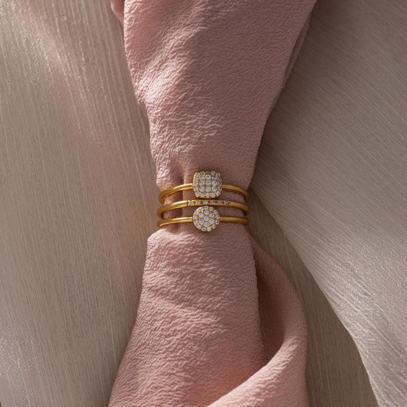 May include: Three gold rings with a square-shaped cluster of small clear stones on each ring.