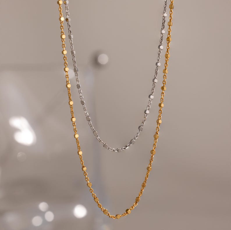 Close-up of two Dot Station Necklaces in silver and gold, each featuring a dainty beaded chain design.