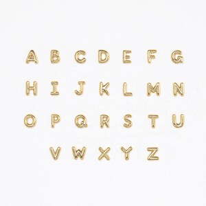 Gold bubble initial stud earrings arranged in a full A to Z alphabet set, displayed in neat rows on a clean white background, highlighting the polished rounded letter design and available options.