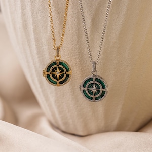 May include: Two round pendant necklaces featuring a green malachite inlay with a central star compass design. One necklace is gold-toned and the other is silver-toned, both with pavé-set stones along the circular frame and the pendant bail.